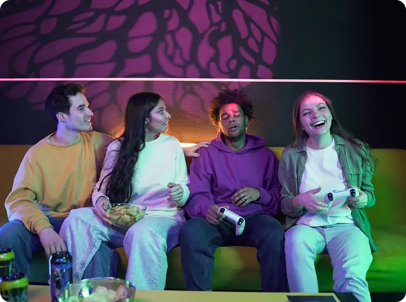 Een groep vrienden zit op een bank en speelt samen videogames op een spelcomputer in een met neon verlichte kamer.